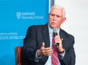 Mike Pence speaks into a microphone, gesturing, against a blue backdrop.