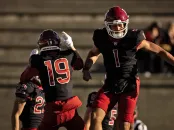 Two Harvard football players celebrate a play, with one jumping excitedly in a stadium.