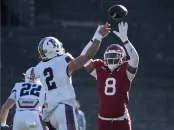 Harvard football player in red attempts to block a pass from a Penn player in white during a game.