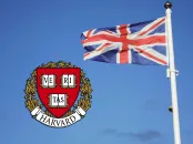 Union Jack flag waving next to the Harvard University crest against a blue sky.
