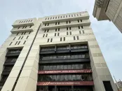 Tall modern building with multiple floors and large windows against a cloudy sky.