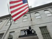 John Harvard statue beneath a large American flag outside of University Hall