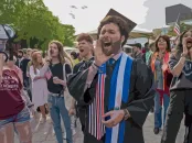 A jubilant graduate shouts into a megaphone, surrounded by a cheering crowd.