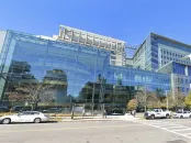 Modern glass building with reflective windows and trees, clear blue sky above.