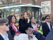 A group of elegantly dressed individuals poses near a parade trolley, smiling and celebrating.