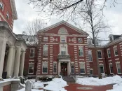 Brick building with classical architecture, surrounded by snow and bare trees.