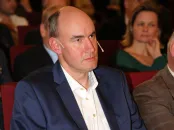 Martin Nowak in a suit attentively listens during a conference, seated among an audience.