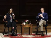Tina Fey and Robert Carlock seated on stage, engaged in conversation with a small table between them.