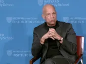 A discussion panel featuring two speakers seated in chairs, with a blue backdrop and an American flag.