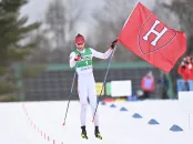 Skier holding a Harvard Crimson flag points at the camera