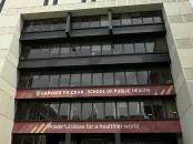 Tall building with multiple stories and large windows, under a cloudy sky.