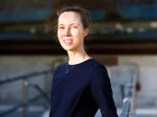 Woman in a navy dress smiling while standing on a walkway with a blurred background.