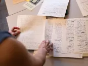 A person examining handwritten notes and papers on a table.