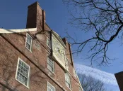 Brick building with a large clock and tree branches against a clear blue sky.