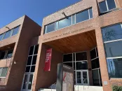 Modern brick building with large windows and an entrance canopy, displaying a red banner.