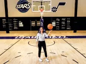 Katie Benzan stands on a basketball court holding a ball, with a hoop in the background.
