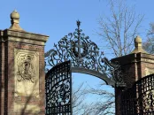 Wrought iron gates with ornate design, framed by brick pillars against a clear blue sky.