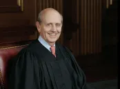 A smiling judge wearing a black robe, seated in a wood-paneled courtroom.