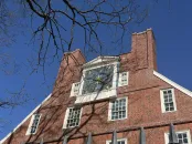 Massachusetts Hall under a clear blue sky, showcasing a prominent clock and large windows.