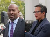 Two men in professional attire, one speaking at a microphone, the other gesturing while talking.