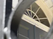 View of a building door labeled "University Hall" through a circular black railing frame.