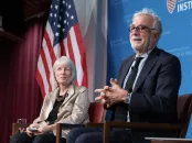 Two figures sitting against an American flag having a conversation at Harvard Kennedy School