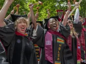 Graduates celebrate with joy, wearing caps and gowns, in a vibrant outdoor setting.