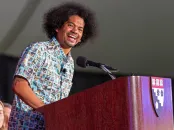 A man smiles while speaking at a podium with a Harvard logo.