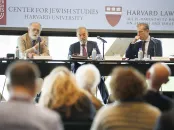Three speakers at a panel discussion in front of an audience, with Harvard branding.