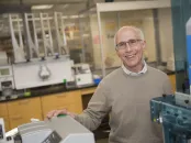 Smiling man with glasses in a laboratory, standing beside equipment.