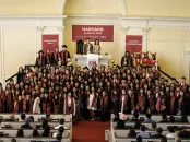 Graduating class posing together in a Harvard ceremony, wearing caps and gowns.