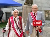 Older woman in a white outfit with a cane and red sash, alongside an elderly man in a gray suit holding a sign.