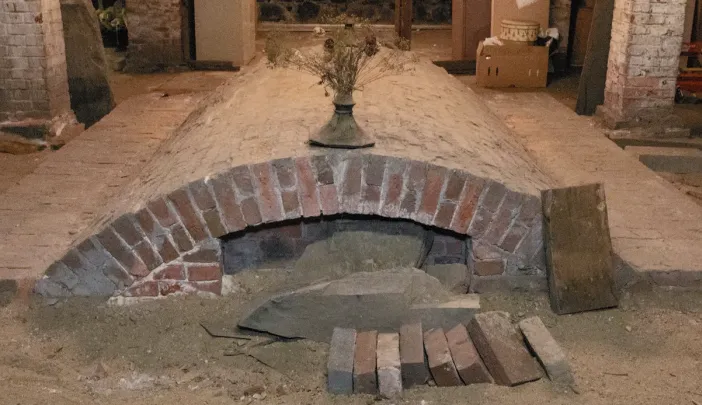 Brick archway with a sandy base, surrounded by wooden planks and boxes in a dim space.