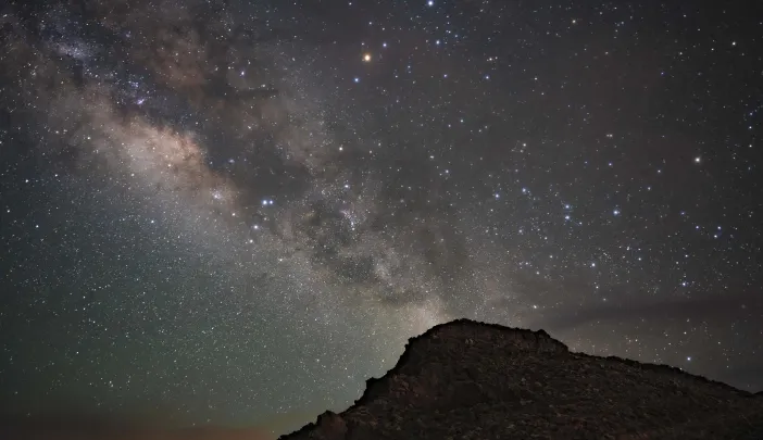 Star-filled night sky with the Milky Way arching over a rocky silhouette.