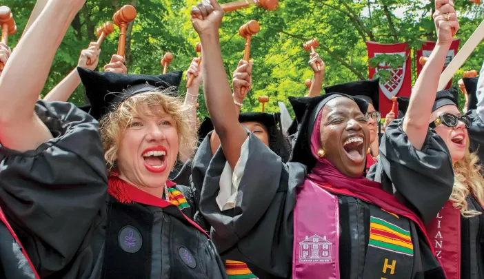 Graduates in caps and gowns celebrate joyfully, raising their hands in excitement.