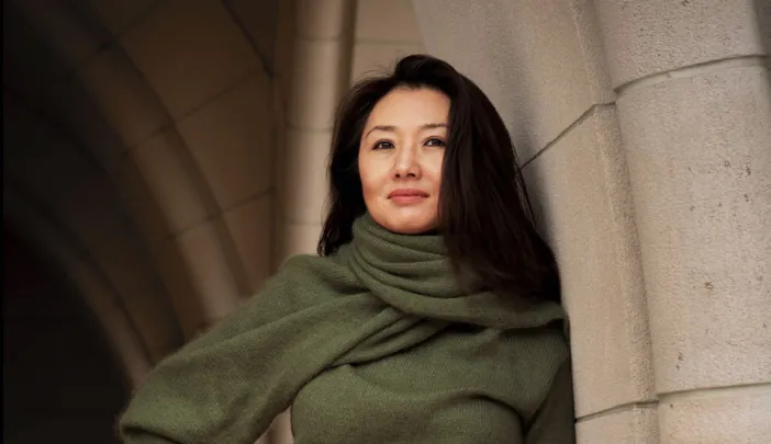 Portrait of Jeannie Suk Gersen, an elegantly dressed Korean American woman leaning against a stone archway.