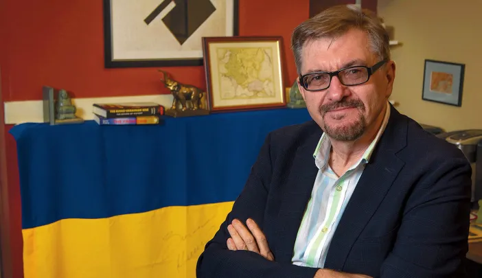 Serhii Plokhy in his Harvard office, smiling with his arms crossed. Behind him hangs a Ukrainian flag signed by Kyiv mayor Vitali Klitschko