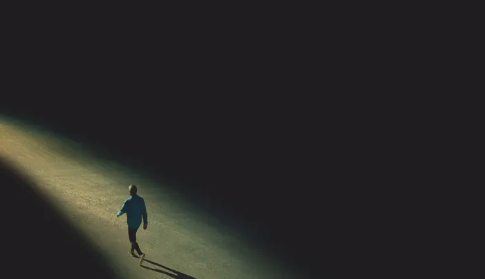 Drawing of a distant solitary figure walking alone toward the horizon along a narrowing path of light edged on both sides by darkness