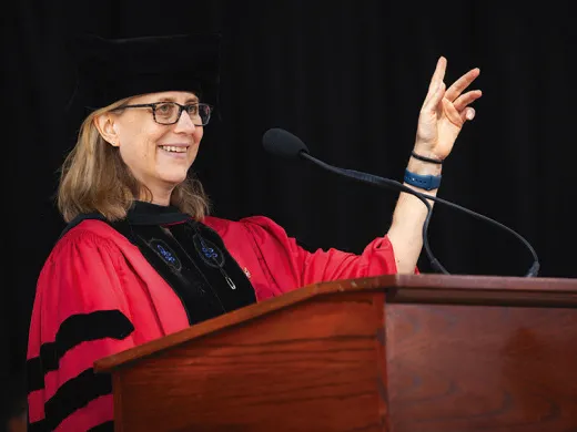 Amanda Claybaugh in academic robes and cap speaking at a podium