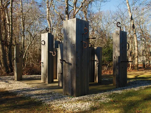 Wooden pillars with curved metal hooks arranged in an outdoor installation.