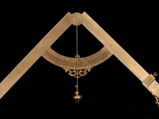 An antique brass plumb level with engraved markings, a curved scale, and a hanging plumb bob against a black background.