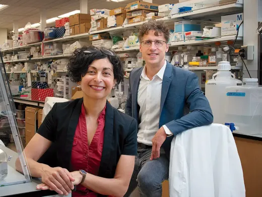 Two laboratory researchers, one seated and one standing, in a scientific lab with equipment.