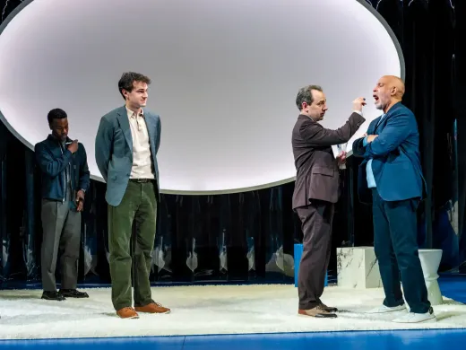 Three actors perform on stage, with one actor interacting closely with another, set against abstract backgrounds.