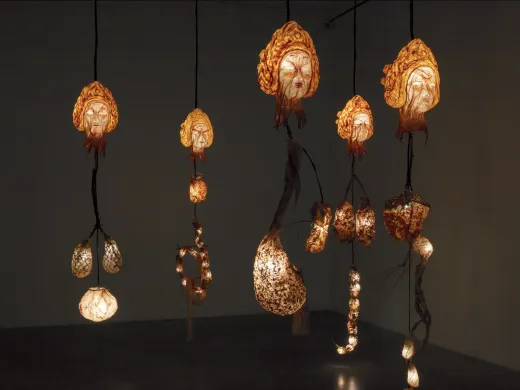 Illuminated hanging sculptures resembling organic forms, casting warm light in a dim space.