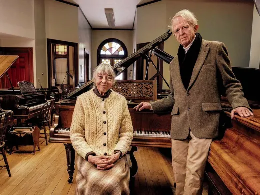 An older couple standing in a large room filled with pianos