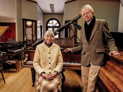 An older couple standing in a large room filled with pianos