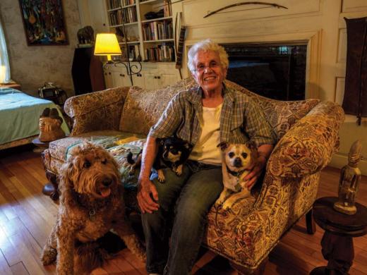 Elizabeth Thomas shown on her couch at home with her own small dogs, Chapek and Kafka, and her son’s large dog, Clover, whom she watches when he is away.