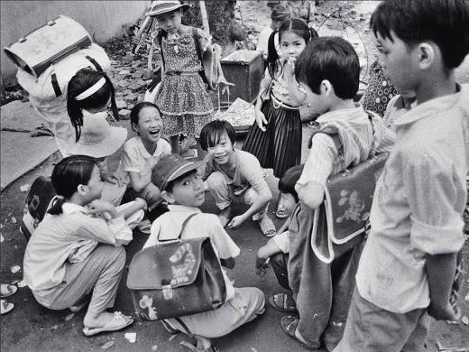 Black and white photo of a group of Vietnamese children, titled “Schoolchildren Playing Cards”