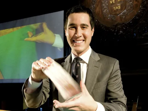 David Kwong shuffles the cards. Behind him, a video gives a closer look at his hands.