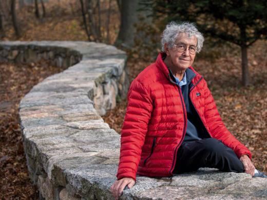 David Roberts seated outdoors on a stone wall by the Charles River